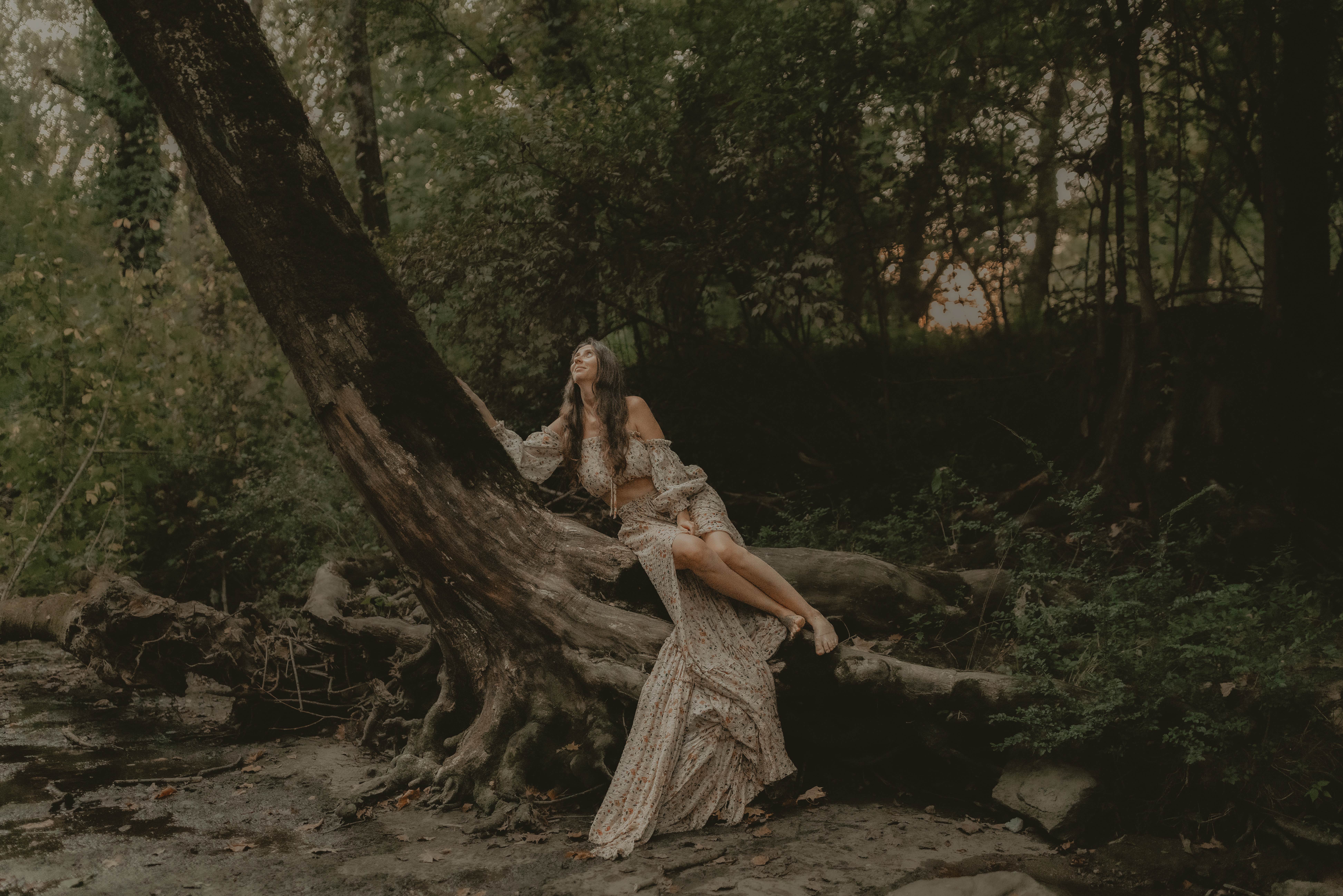 Theresa sitting on a fallen tree in a wooded creek bed
